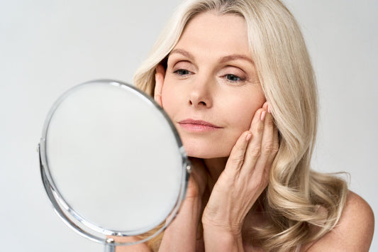 Senior woman looking in mirror to see effects of cbd skincare treatment for seniors